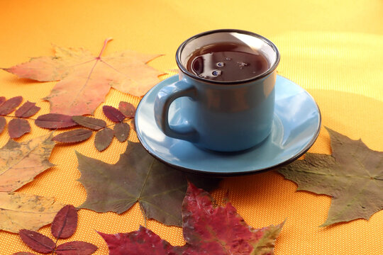 Scattered dry leaves with a mug of hot tea on a yellow background in the sun, side view, close-up