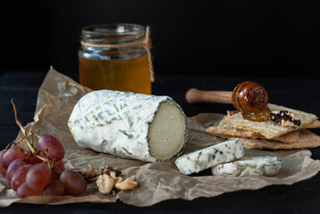 Fototapeta premium Delicious goat chevre cheese slices with grapes, honey and nuts on a dark wooden background.