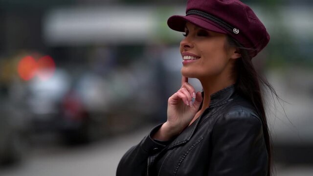 Beautiful female model in a purple cap and leather jacket she poses in a public place. Located on a street in the city.
