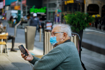 Obraz premium Old man using mobile phone on New York City in wearing face mask as protection against covid-19 flu virus new normal, pandemic.