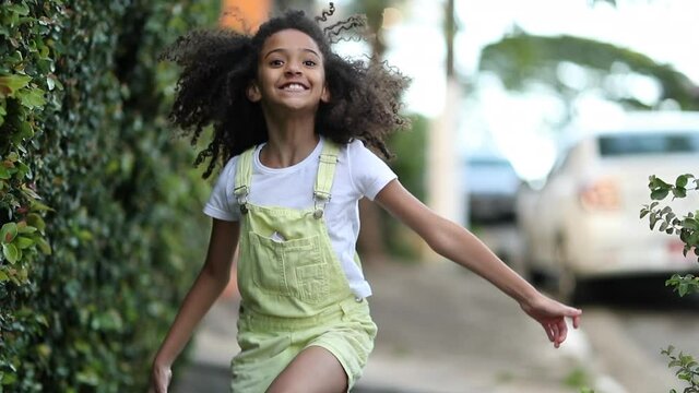 Happy little girl running outside in sidewalk. Mixed race black child feeling jow in slow-motion run