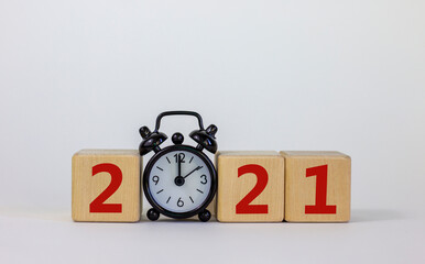 Business concept of 2021 new year. Wooden cubes and black alarm clock, number 2021. Beautiful white background, copy space.