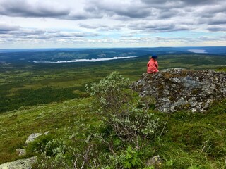 A Swedish girl looking out over a great rural area. From a mountain or hill. Plenty of clouds in the sky. Ansätten, Jämtland, Sweden.
