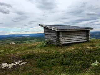 Fototapeta na wymiar A small wooden cabin at a top of a mountain. Great view over a Swedish landscape. Plenty of clouds this gray day. No sun. Ansätten, Jämtland, Sweden.