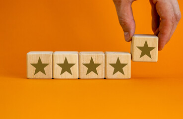 Wood cubes with gold star signs on beautiful orange background, copy space. Male hand. Quality and...