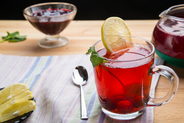 Berry tea in a cup next to a teapot spoon and jam lemon and lemon balm on a napkin top view.