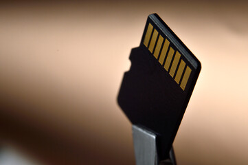 Close-up of a Micro SD memory card against a golden gradient background, clamped with tweezers.