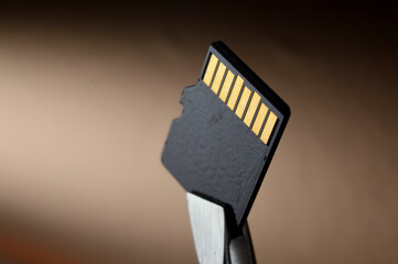 Close-up of a Micro SD memory card against a golden gradient background, clamped with tweezers.