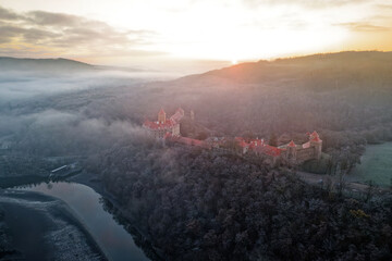 Aerial view of the large and beautiful Moravian royal castle Veveri (Burg Eichhorn), standing on a rock above water dam on the river Svratka, early morning light and autumn weather with the green fore - obrazy, fototapety, plakaty