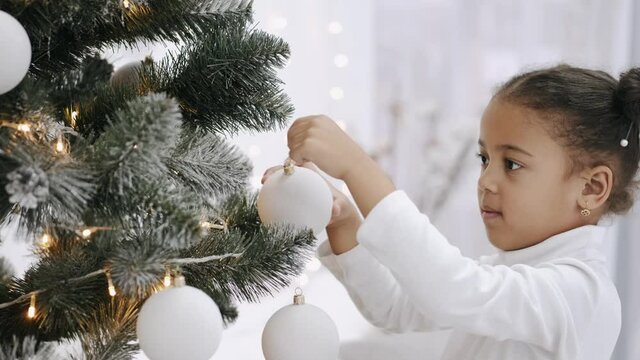 Kids on winter holidays. Family time. A little cute girl is decorating Christmas tree at home.
