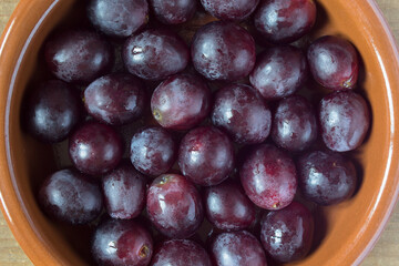 Overhead view of a round rustic clay bowl filled with black seed grapes. Organic and healthy fruit.