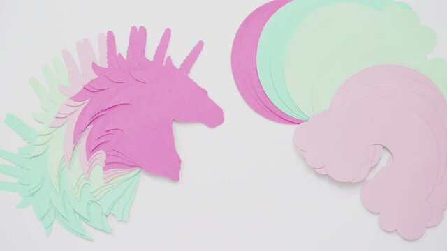 Time lapse. Flat lay. Colorful unicorn paper cutouts on a white background.
