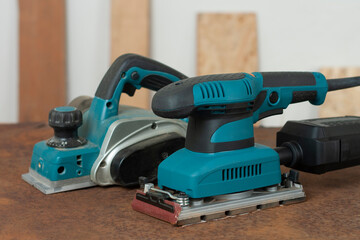 Electric planer and electric sheet finishing sander on old rusty metal sheet, on background...