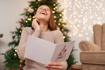 Beautiful woman laughing while reading a Christmas greeting card with light in background. Copy...