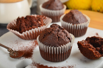 Chocolate muffin on a white marble board next to other muffins sprinkled with cocoa.