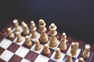 wooden white and black chess pieces on the board. blurry background. 
