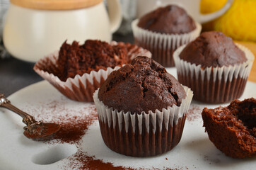 Chocolate muffin with a crack on top, sprinkled with cocoa on a white marble board.