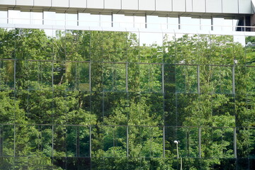 A cutout of a  modern building with a glass facade. There are trees reflecting in the facade making...