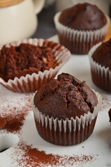 Chocolate muffin with a crack on top, sprinkled with cocoa on a white marble board.