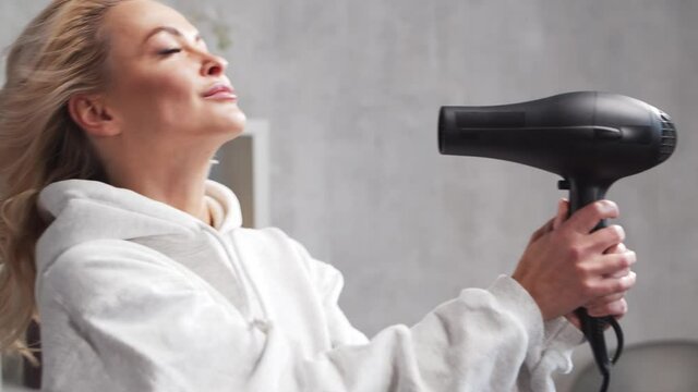 Young woman having fun and dancing, drying her hair with a hairdryer at home.