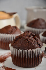Chocolate muffin with a crack on top, sprinkled with cocoa on a white marble board, on the grey background.