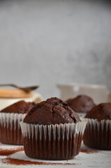 Chocolate muffin with a crack on top, sprinkled with cocoa on a white marble board, on the grey background.
