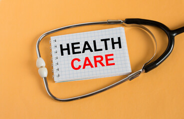 Notepad with text Health Care lies with a stethoscope on an orange background
