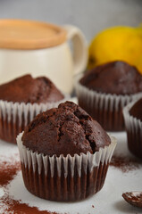 Chocolate muffin on a white marble board next to other muffins sprinkled with cocoa.