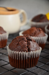 Chocolate muffin with a crack on top on a black metal grate on a black background.
