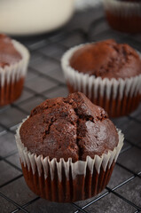 Chocolate muffin with a crack on top on a black metal grate on a black background.
