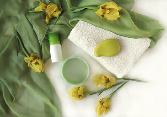 Body care products with a white bath towel and scattered yellow iris flowers on a light fabric, top...