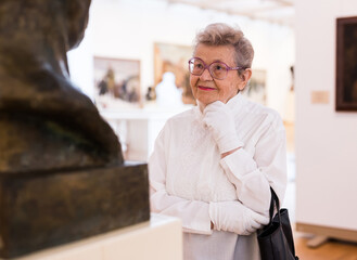 mature woman  examines sculpture in an exhibition in hall of an art museum
