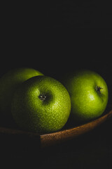 MANZANAS VERDES SOBRE PLATO DE MADERA Y FONDO NEGRO