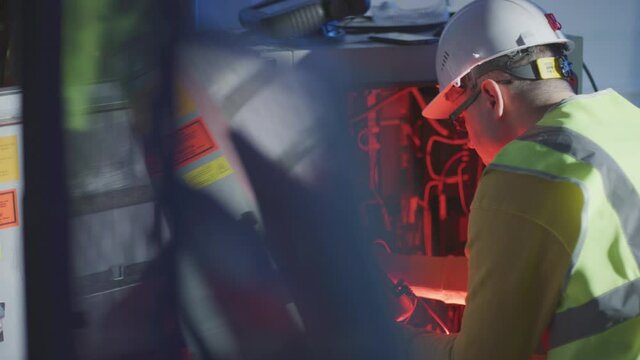 Service engineer or electrician works with industrial robot cabinet and electrical tester