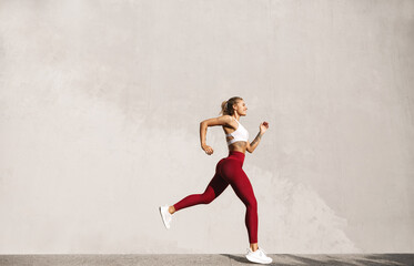 Healthy young woman running in morning. Fitness model exercising outdoors. Full length side view...