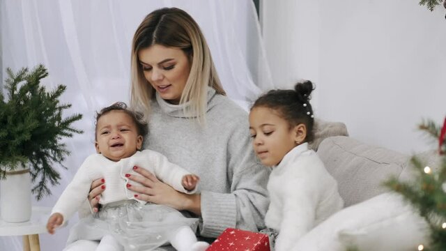 Family celebrating Christmas holidays at home. Pretty moher with her lovely kids are sitting on a sofa near xmas tree.