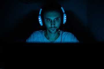 Un chico joven en una habitación oscura jugando al ordenador o trabajando como hacker con su...