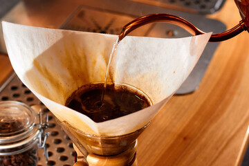 Making drip coffee. Barista pours hot water from a copper kettle through fresh ground coffee into the paper filter. Chemex.