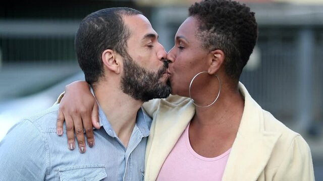 Mixed race couple kissing eath other outside and smiling at camera