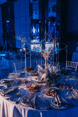 Wedding table setting and decoration. Cutlery on the table. Floral decorations in the banquet hall. Blue background.
