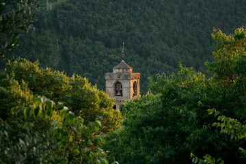 Fototapeta na wymiar Great view of the bell tower of San Pedro church among the lush vegetation, in the town of Boltaña, in the Aragonese Pyrenees (Huesca, northern Spain)
