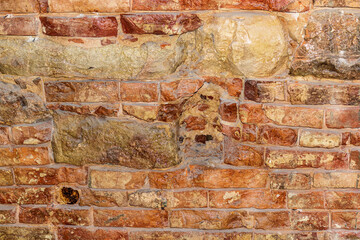 An abstract fragment of an old unpainted brick wall with the addition of natural stone. The concept of an old brick wall with a cracked surface that is used as a background.