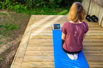 une jeune fille de dos prend des cours de sport à partir de vidéo sur sa tablette, en extérieur