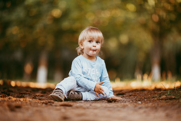 A beautiful young boy in blue clothes is sitting and smiling at someone on an autumn day