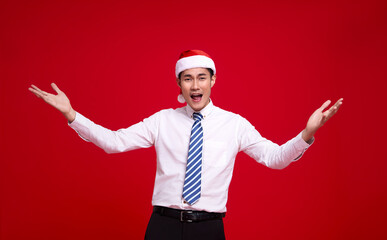 Excited asian business man wearing Santa hat and action open hand gesture  on isolated over red background.Happy new year concept.