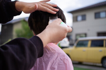 庭で子供の髪をバリカンでカットしている母親