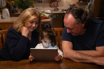 grandparents with their granddaughter sitting at the kitchen table while spending time with a tablet