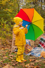 cute beautiful prescholer boy in an orange pants, raincoat, hat, rubber boots with a...