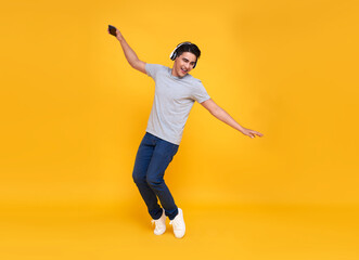 Fototapeta na wymiar Young handsome Asian man smiling and jumping wearing wireless headphone listening to music isolated over yellow background.