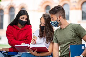 Students studying together sitting on a bench outdoor and wearing masks during coronavirus times